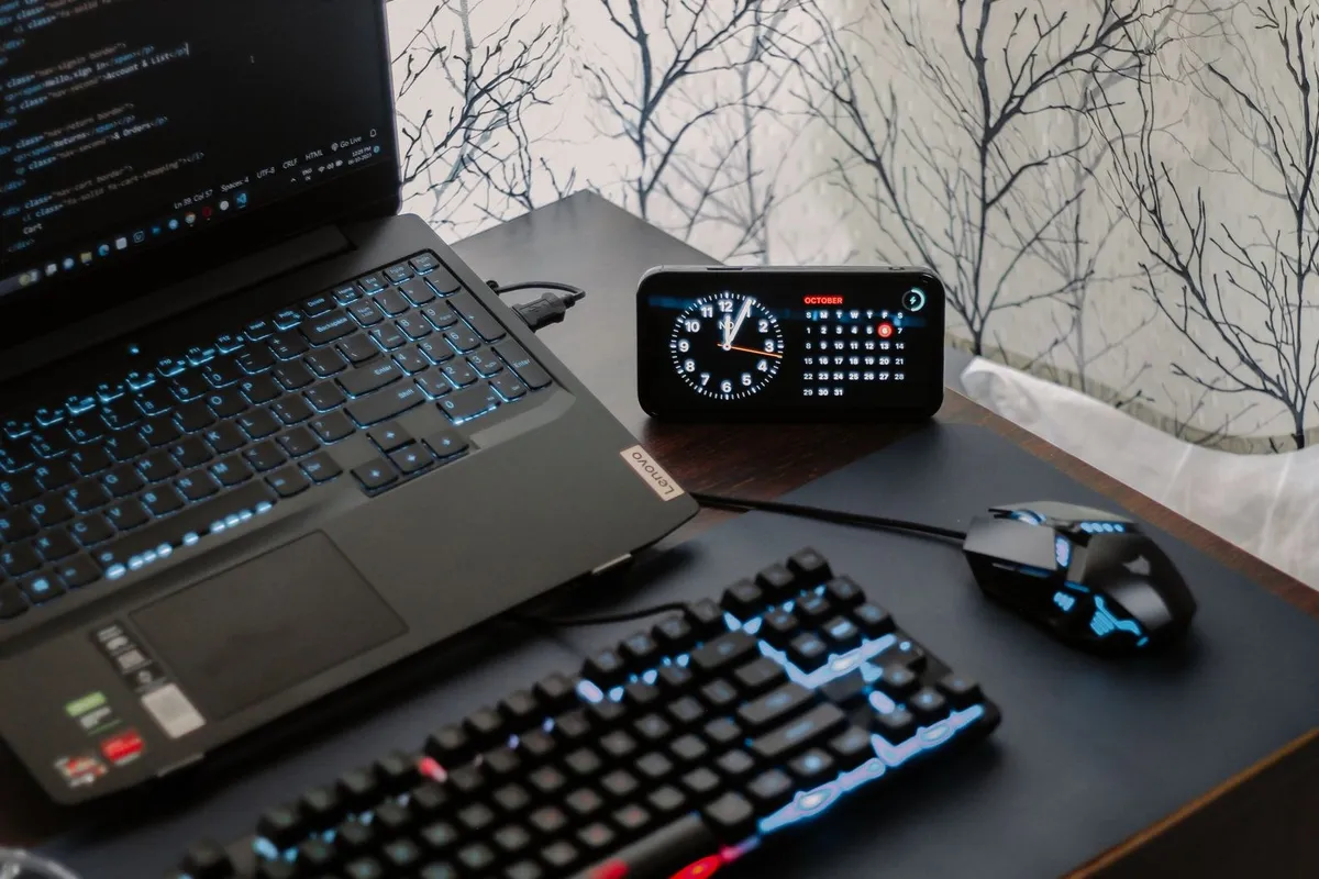 A modern workspace with a laptop, digital clock, and gaming mouse, reflecting a tech-savvy environment.