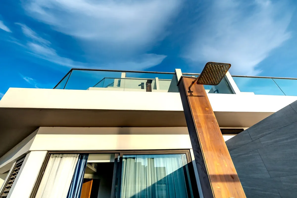 A modern terrace featuring glass railings and an outdoor shower under a bright sky, symbolizing quality design.